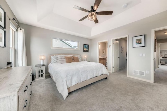 bedroom with visible vents, a tray ceiling, connected bathroom, baseboards, and light colored carpet