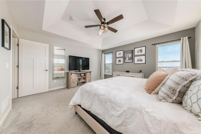 bedroom featuring baseboards, a raised ceiling, light colored carpet, and ceiling fan