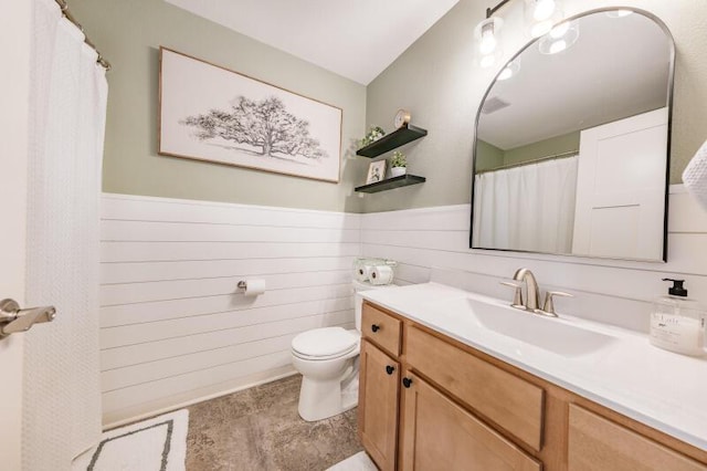 full bath featuring a wainscoted wall, wooden walls, toilet, and vanity