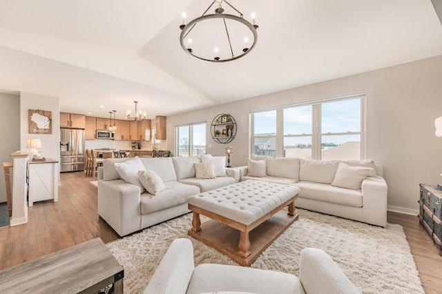 living area featuring a notable chandelier, light wood-style flooring, baseboards, and vaulted ceiling