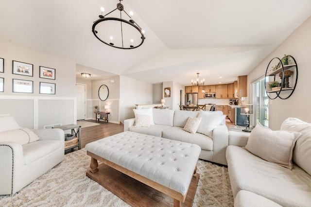 living area with an inviting chandelier, light wood-style flooring, and vaulted ceiling