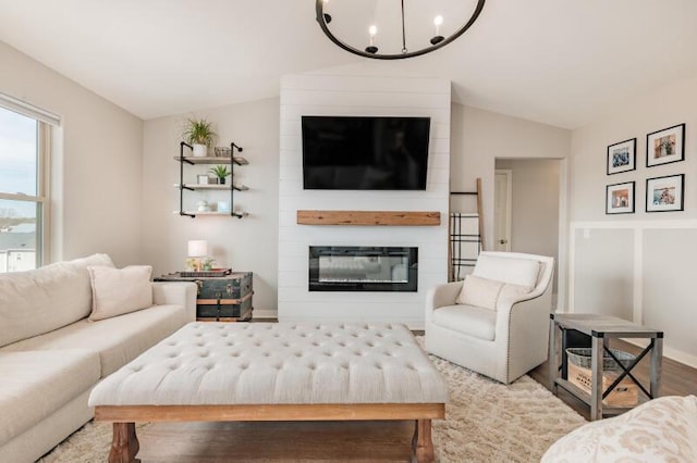 living room with a large fireplace, an inviting chandelier, wood finished floors, and vaulted ceiling