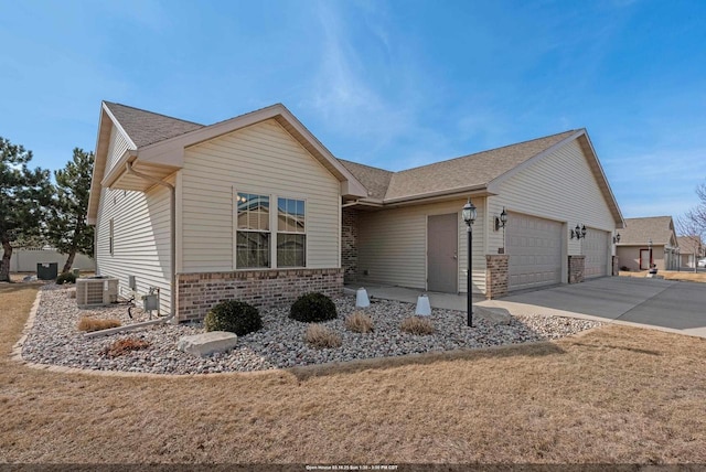 ranch-style house featuring brick siding, concrete driveway, a front yard, central AC unit, and an attached garage