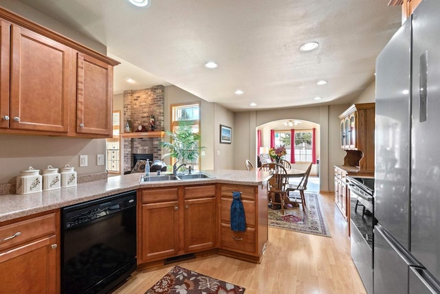 kitchen with a peninsula, a fireplace, a sink, stainless steel appliances, and brown cabinets