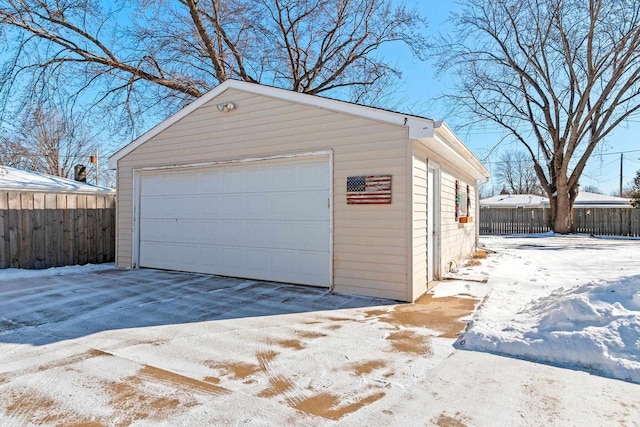 snow covered garage with a detached garage and fence