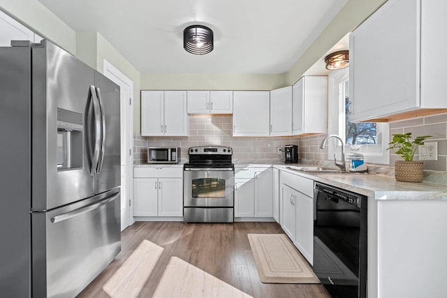 kitchen featuring light wood finished floors, a sink, decorative backsplash, appliances with stainless steel finishes, and white cabinetry