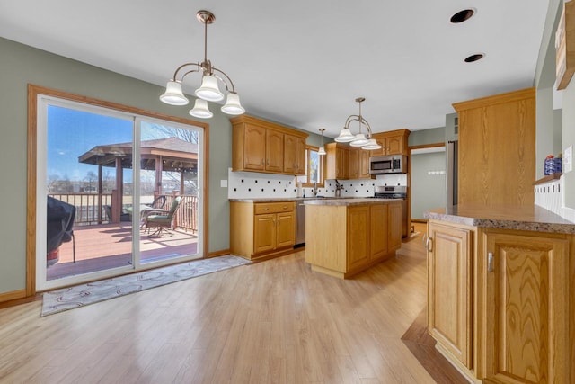 kitchen featuring an inviting chandelier, light wood-style flooring, stainless steel appliances, decorative backsplash, and pendant lighting