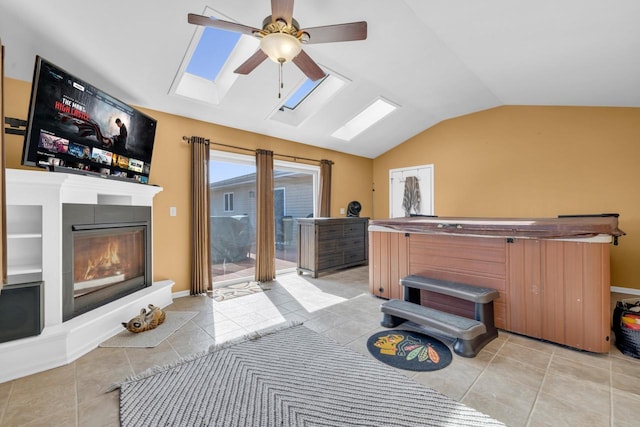 interior space featuring baseboards, lofted ceiling with skylight, light tile patterned floors, a glass covered fireplace, and a ceiling fan