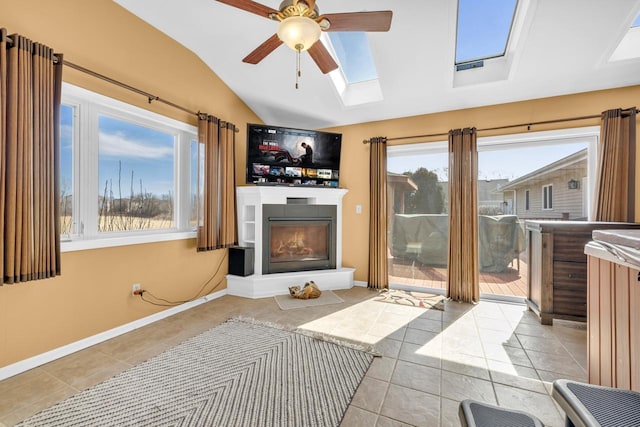 tiled living room with a glass covered fireplace, lofted ceiling with skylight, baseboards, and a wealth of natural light