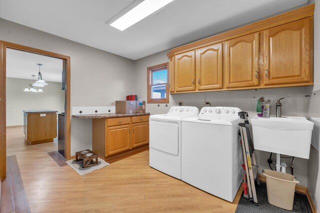 clothes washing area featuring a sink, cabinet space, independent washer and dryer, and light wood finished floors