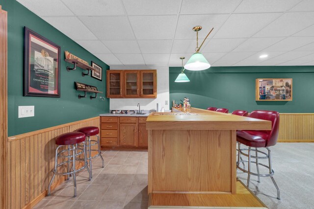 kitchen featuring a kitchen breakfast bar, a paneled ceiling, a wainscoted wall, and a sink