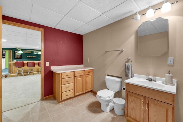 bathroom with vanity, baseboards, a paneled ceiling, tile patterned floors, and toilet