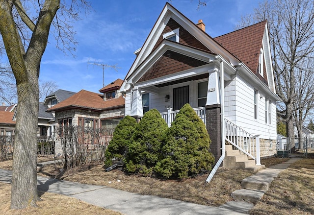 view of front of house with covered porch, a chimney, and fence