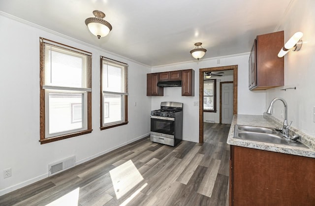 kitchen with stainless steel gas range oven, visible vents, dark wood finished floors, under cabinet range hood, and a sink