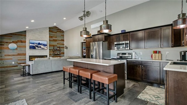 kitchen featuring open floor plan, appliances with stainless steel finishes, a stone fireplace, and high vaulted ceiling