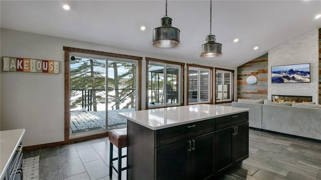 kitchen with a stone fireplace, a breakfast bar area, light countertops, dark cabinets, and vaulted ceiling