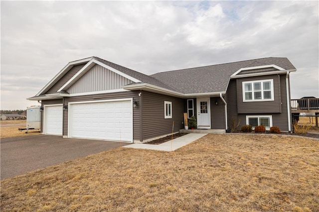 tri-level home with a front lawn, an attached garage, driveway, and a shingled roof