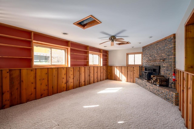 unfurnished living room featuring a ceiling fan, visible vents, carpet floors, a wood stove, and wood walls