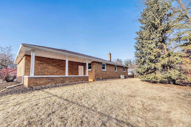 back of house featuring brick siding, central air condition unit, and a chimney