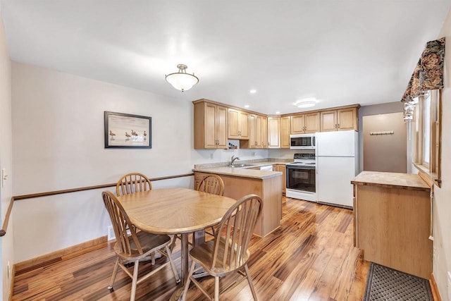 kitchen featuring light countertops, light wood-type flooring, a peninsula, white appliances, and a sink