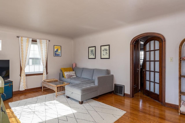 living room featuring wood finished floors, visible vents, arched walkways, and baseboards