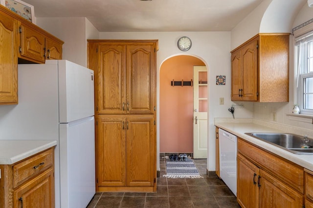 kitchen featuring white appliances, brown cabinetry, light countertops, and a sink