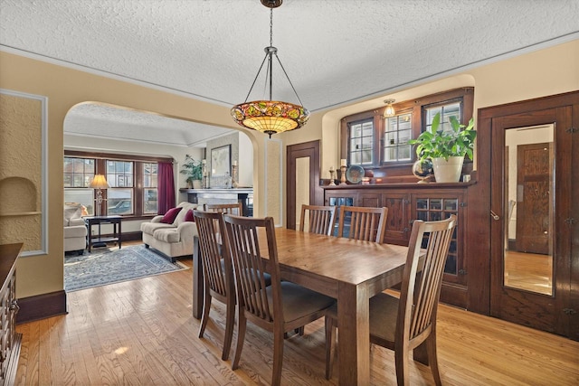 dining space with a wealth of natural light, arched walkways, and light wood-style floors