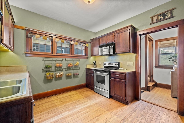 kitchen featuring a sink, stainless steel electric stove, light wood-style floors, black microwave, and light countertops