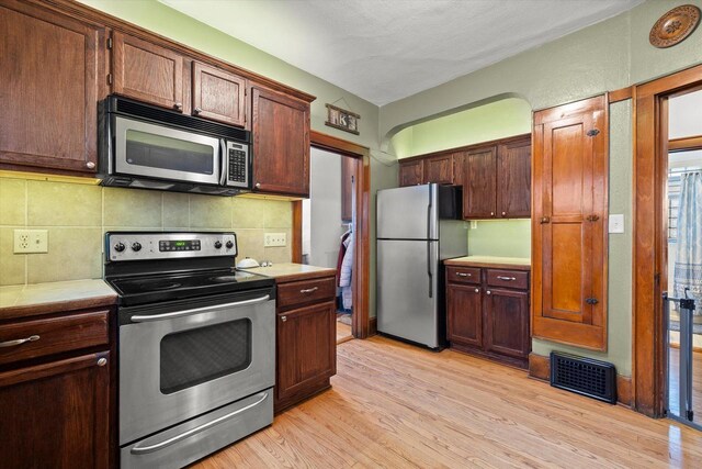 kitchen featuring stainless steel appliances, tasteful backsplash, visible vents, and light wood finished floors