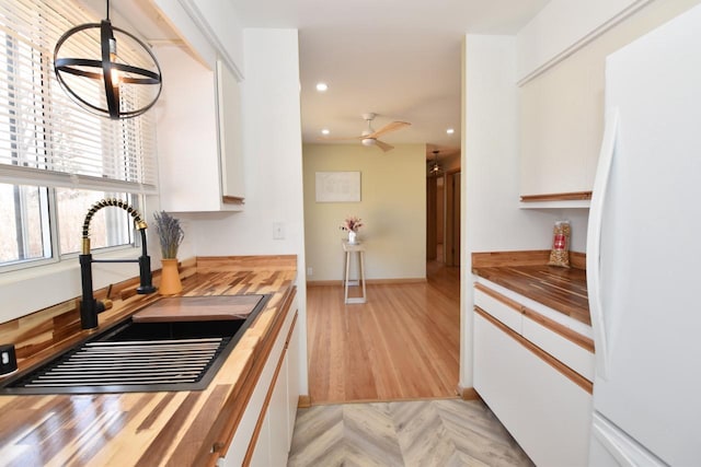 kitchen with butcher block counters, white cabinetry, freestanding refrigerator, and a sink