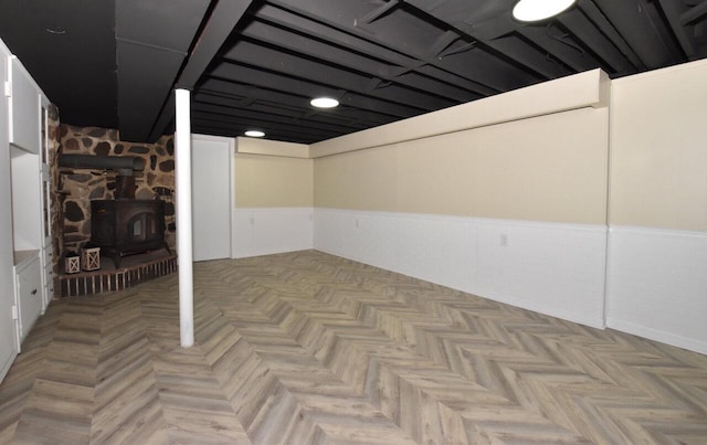 finished basement featuring a wainscoted wall and a wood stove