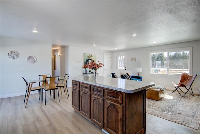 kitchen featuring light wood-style flooring, a textured ceiling, a center island, light countertops, and baseboards