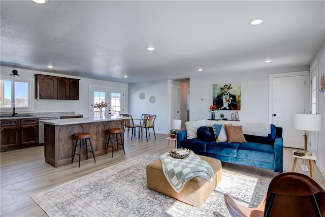 living area with recessed lighting, a textured ceiling, light wood-type flooring, and baseboards