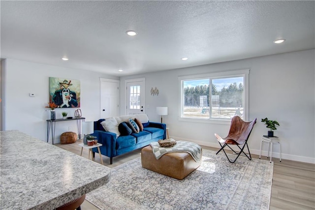 living area featuring recessed lighting, baseboards, a textured ceiling, and light wood-style flooring