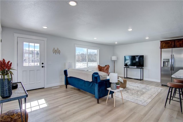 interior space with baseboards, recessed lighting, stainless steel fridge with ice dispenser, light wood-style floors, and a textured ceiling