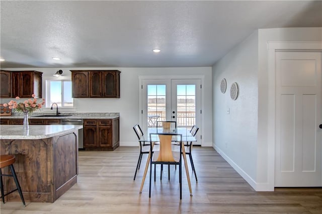 kitchen featuring dishwasher, light wood-type flooring, a kitchen bar, a textured ceiling, and a sink