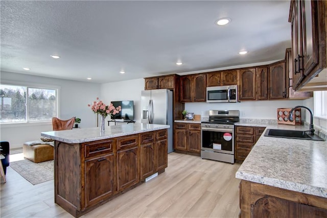 kitchen with a kitchen island, light wood-type flooring, light countertops, stainless steel appliances, and a sink