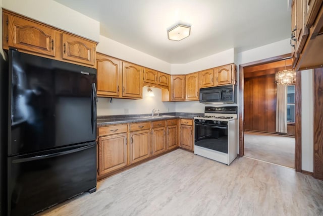 kitchen with dark countertops, light wood-style floors, brown cabinetry, black appliances, and a sink