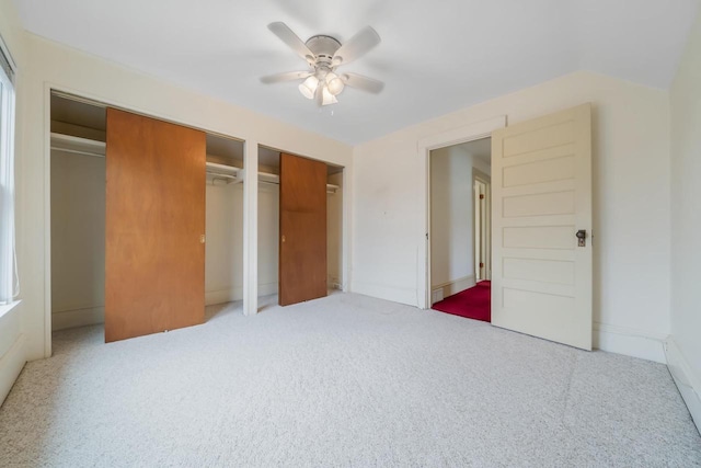 unfurnished bedroom with baseboards, multiple closets, carpet, and ceiling fan