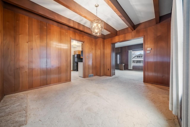 carpeted empty room featuring a chandelier, beamed ceiling, wood walls, and visible vents