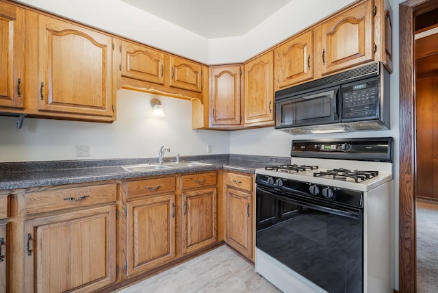 kitchen featuring range with gas stovetop, a sink, black microwave, dark countertops, and brown cabinets