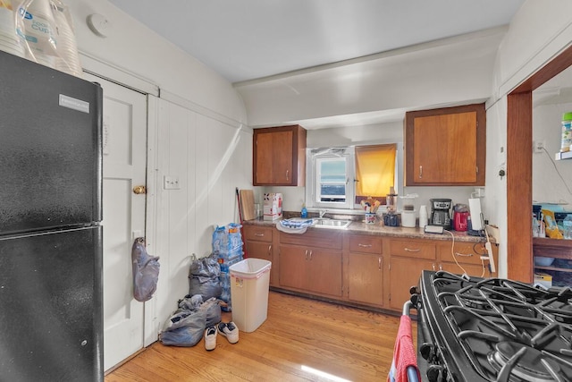 kitchen featuring black appliances, light wood-style floors, brown cabinets, and a sink