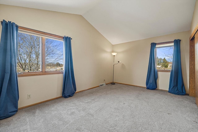 carpeted empty room with a wealth of natural light, visible vents, baseboards, and lofted ceiling