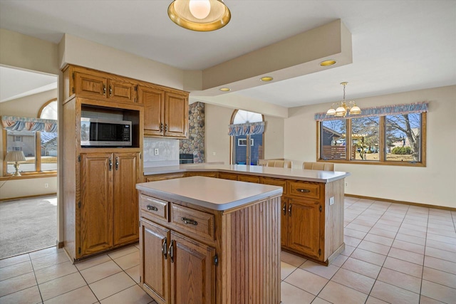 kitchen with light tile patterned flooring, stainless steel microwave, a peninsula, and a kitchen island