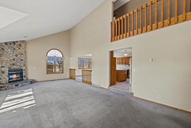 unfurnished living room featuring a stone fireplace, baseboards, carpet floors, and high vaulted ceiling