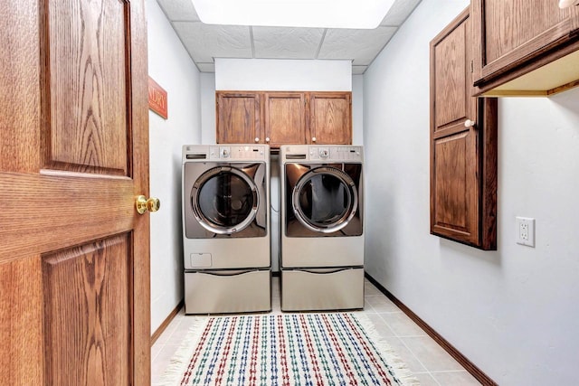 clothes washing area with light tile patterned floors, cabinet space, baseboards, and separate washer and dryer