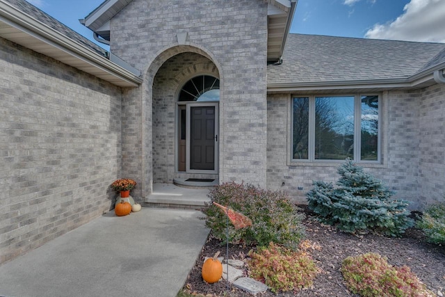 doorway to property featuring brick siding and roof with shingles