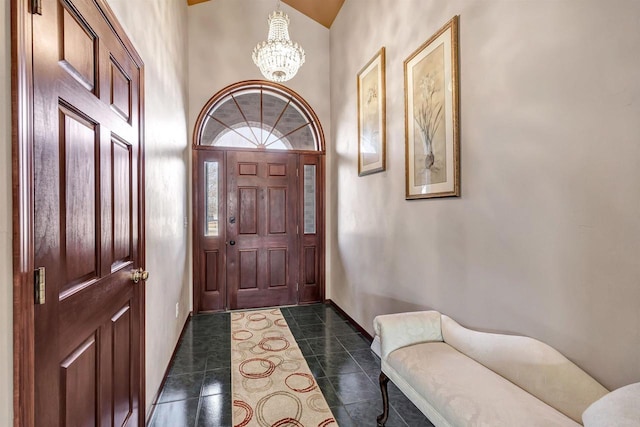 entryway with a notable chandelier, a towering ceiling, baseboards, and dark tile patterned flooring