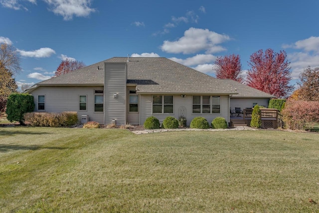 rear view of property with a deck, a lawn, and a shingled roof