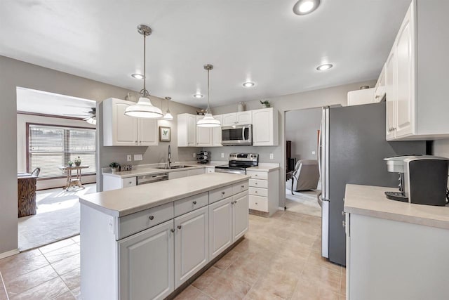 kitchen with a kitchen island, light countertops, appliances with stainless steel finishes, white cabinetry, and a sink